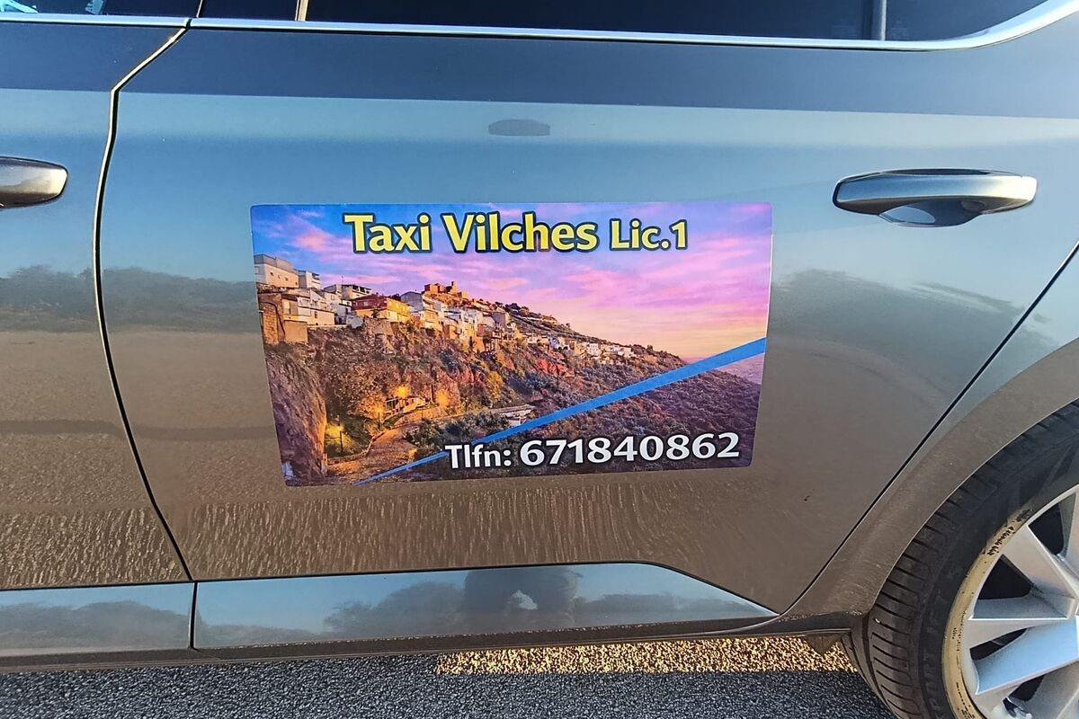 Rótulo Taxi Vilches licencia 1 en la puerta del coche, con una foto del pueblo al atardecer